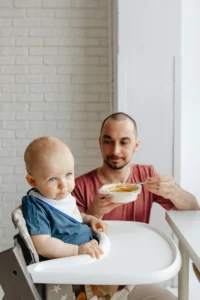 Baby in Blue Shirt Sitting on White High Chair