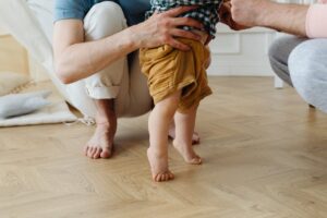 a boy learning walking on floor with support of his father