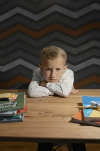 Boy in White Long Sleeve Shirt Resting Head on Wooden Table