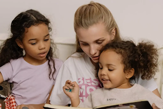 a mother reading a book with her two doughters- Childhood Development Tips in Hindi (Hindi Mein Bachpan Ke Vikas Ke Tips)