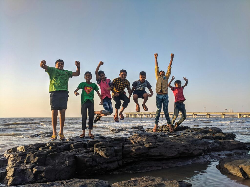 a group of teenage children jumping on a rock near sea sore