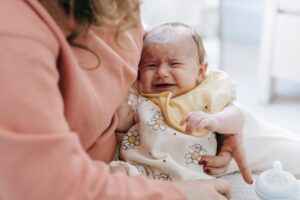 a baby crying due to colic pain on a lap of mother