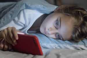 a child watching mobile while sleeping in bed for topic Cyberbullying Meaning in Hindi